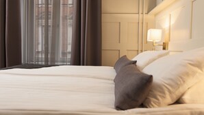 A neatly made bed with white linens and a few pillows, a bedside lamp, and a view of a building through sheer curtains. - Best Western Plus Hotel Baltic (Sundsvall)