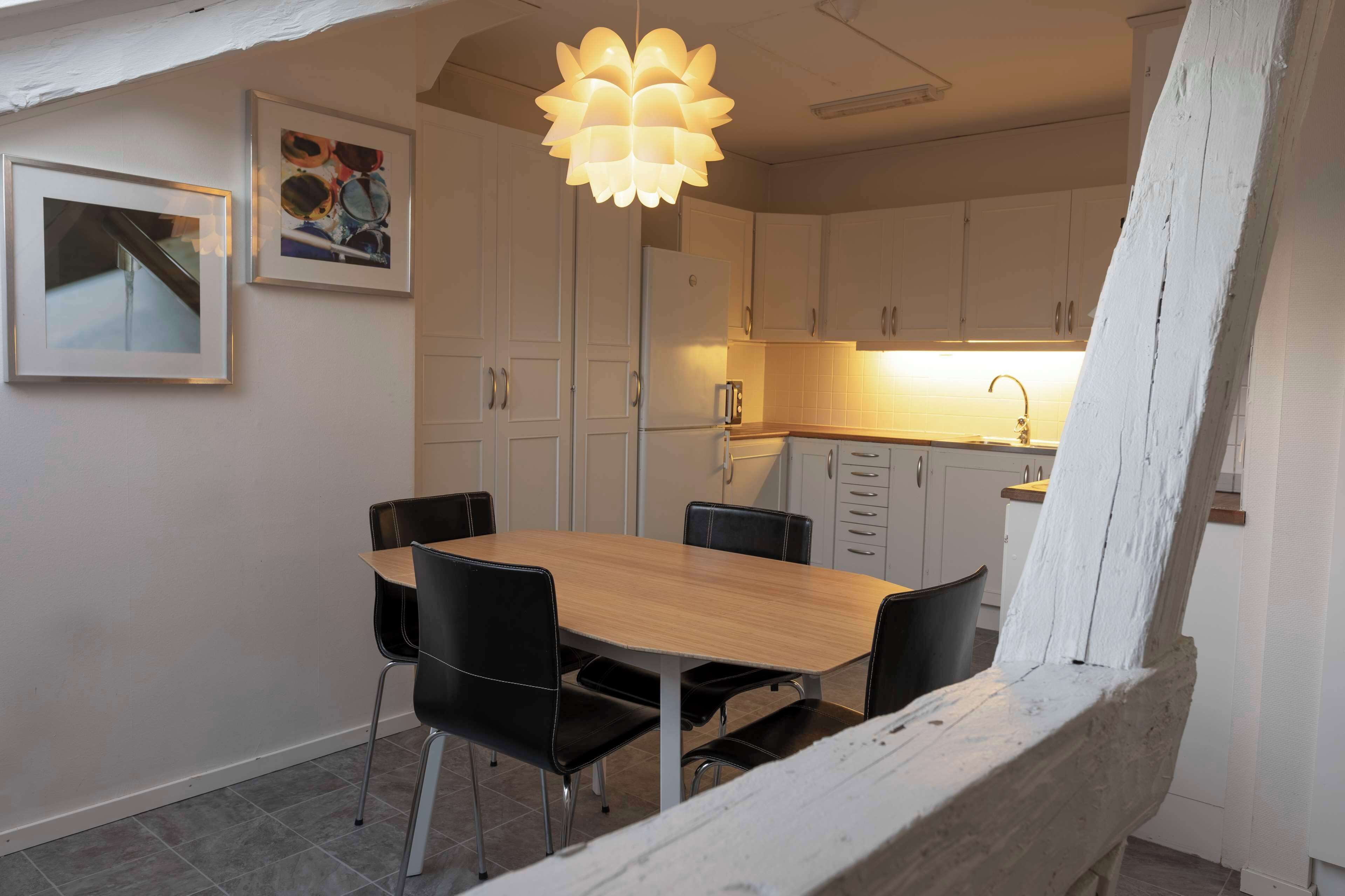 A dining area with a wooden table and black chairs, a pendant light, and white cabinets.