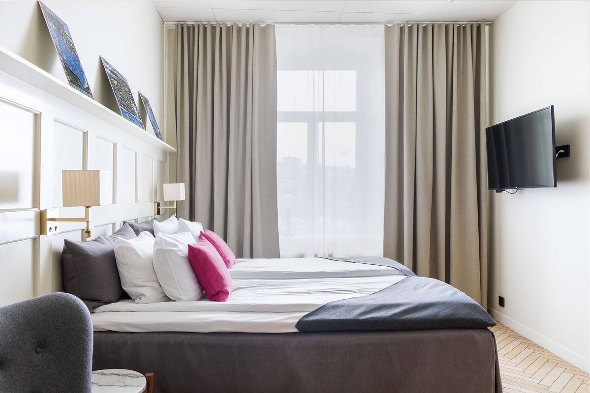 A hotel room with a bed, a chair, a TV, and a window with curtains.