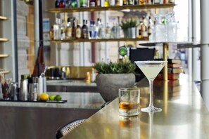 A bar area with a martini glass and a shot glass on a counter, shelves with bottles and a potted plant in the background. - Best Western Plus Hotel Baltic (Sundsvall)