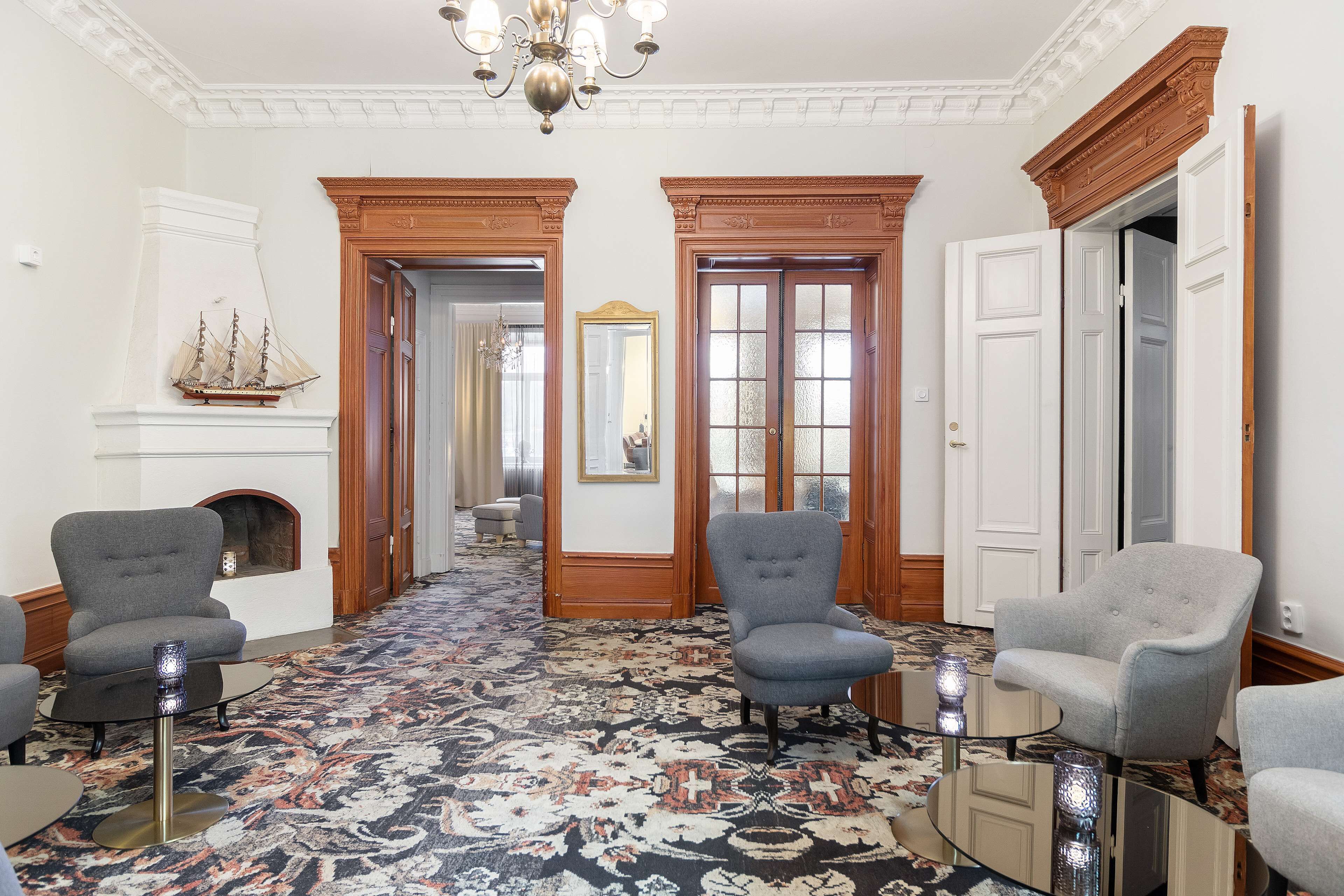 A spacious room with a patterned carpet, two armchairs, a small table, and a fireplace.