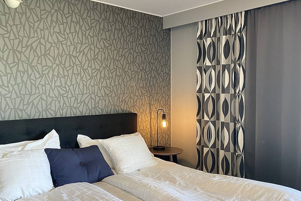A neatly made bed with white and blue bedding, a modern headboard, and a patterned wall.