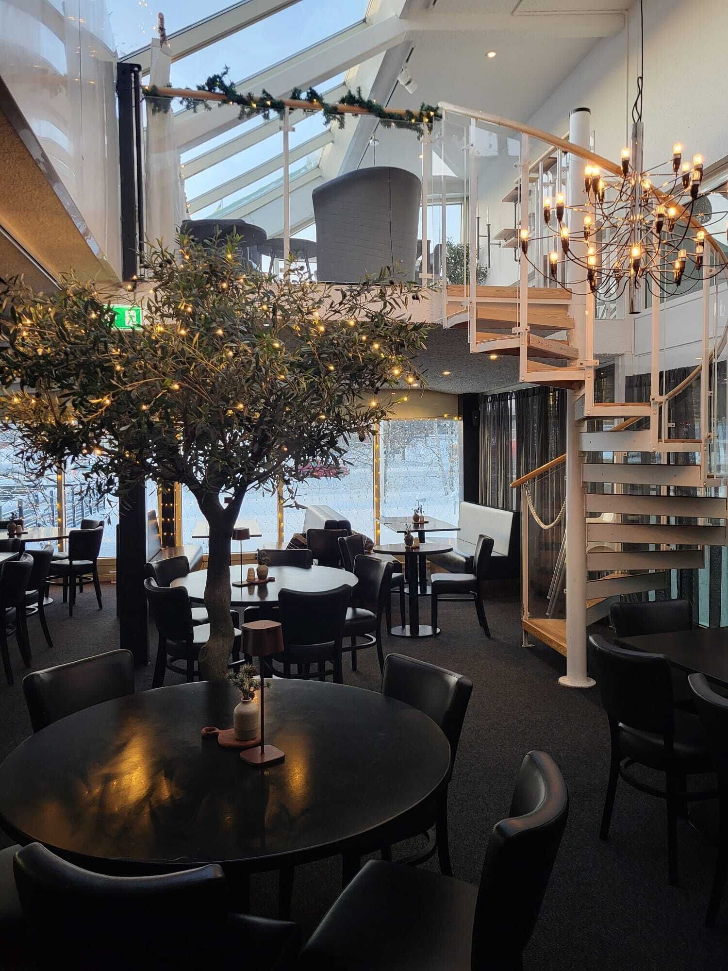 A modern indoor space with a central tree adorned with lights, surrounded by tables and chairs.