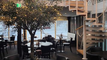 Un ambiente interno moderno con un albero centrale decorato con luci, circondato da tavoli e sedie.