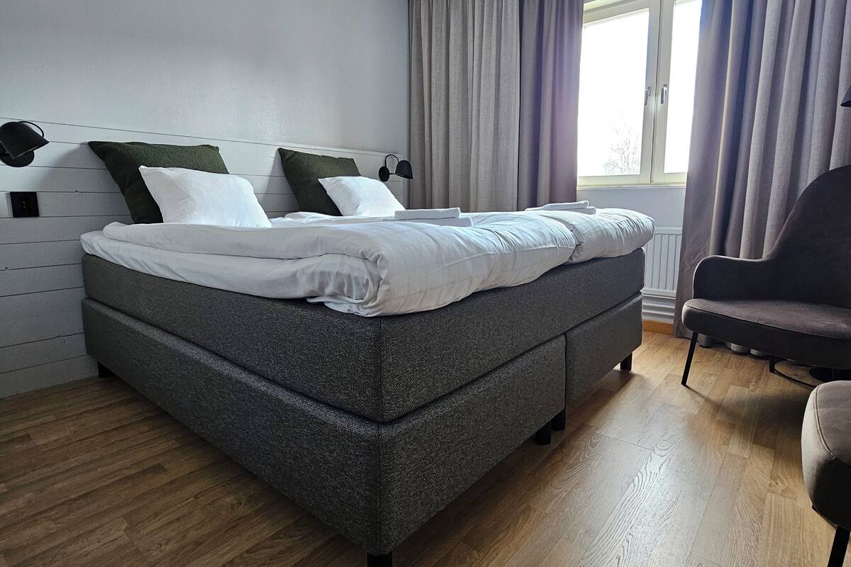 A modern bedroom with a large bed, a chair, and a window with curtains.