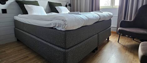 A modern bedroom with a large bed, a chair, and a window with curtains.