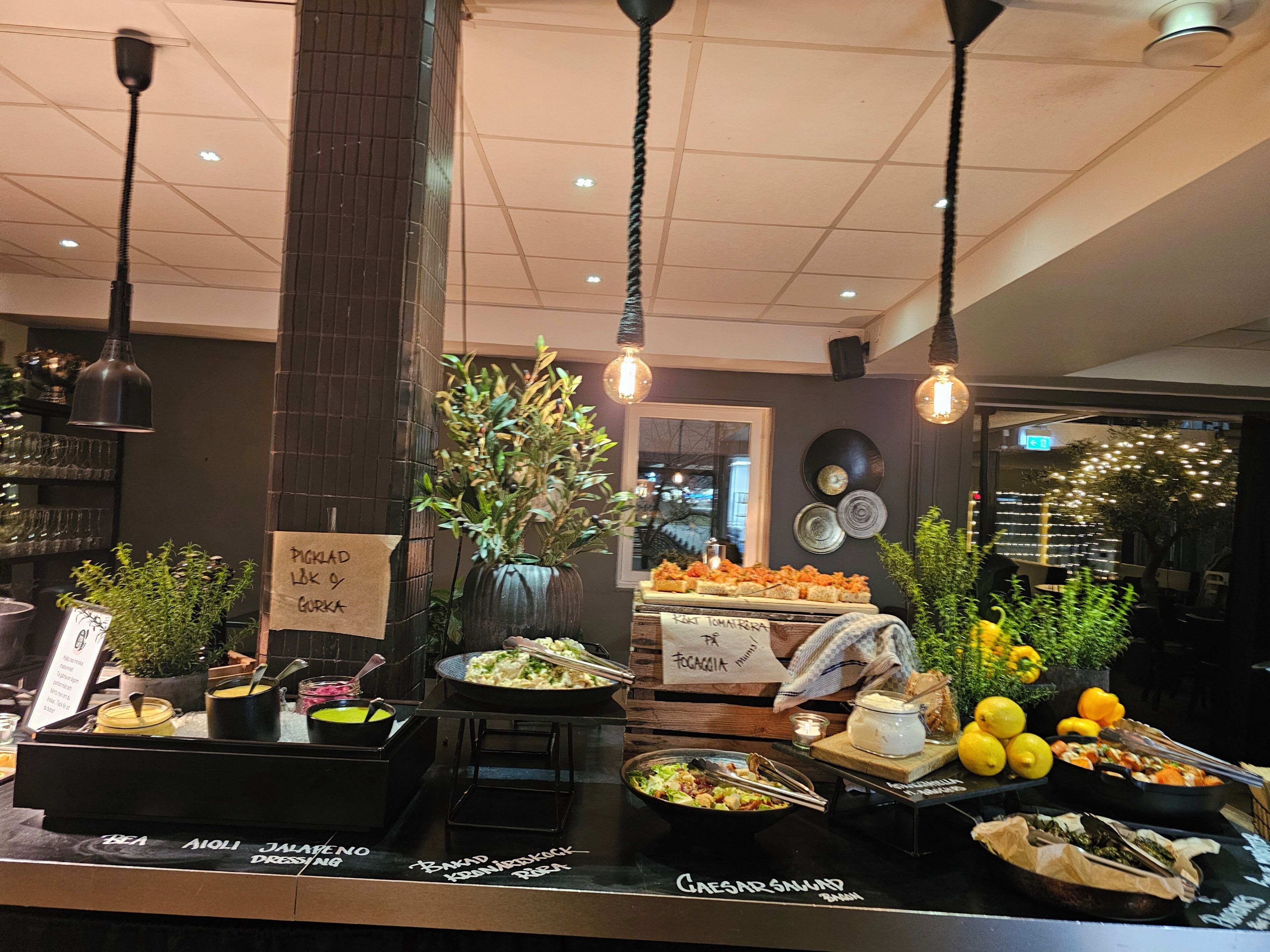 Een buffetruimte met verschillende stations voor eten, waaronder een Caesar salade en een selectie van fruit.