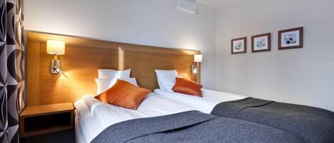 Une chambre d’hôtel avec un lit double, deux tables de chevet, une tête de lit en bois et trois lampes fixées au mur.
