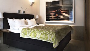 A modern bedroom with a black bed, white pillows, a green patterned throw, a wall-mounted TV, and a framed artwork above the bed. - Anno 1647 (Stockholm)