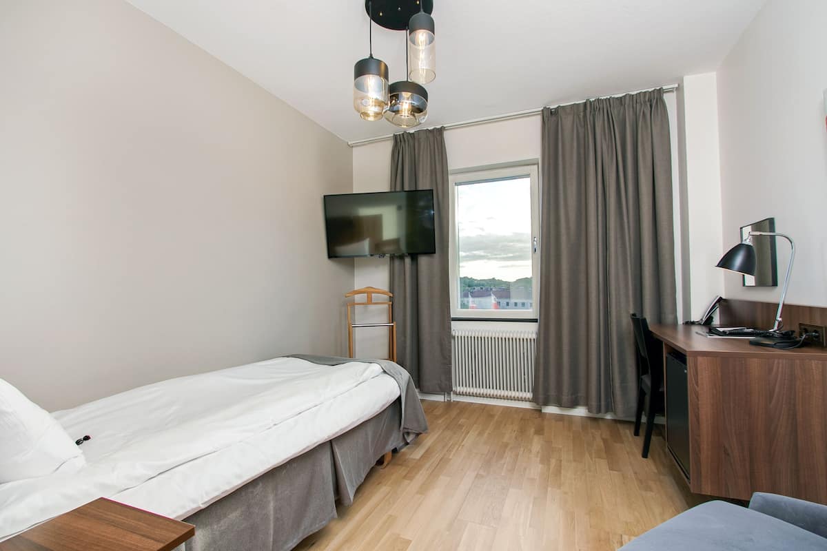 A hotel room with a bed, a desk, a television, and a view of the city.
