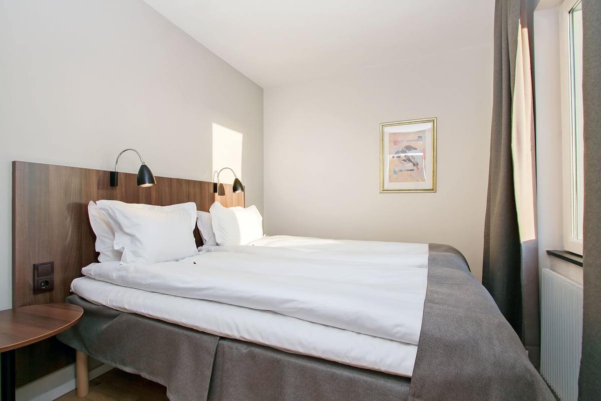 A neatly made bed with white linens, a wooden headboard, and a bedside table with a lamp.