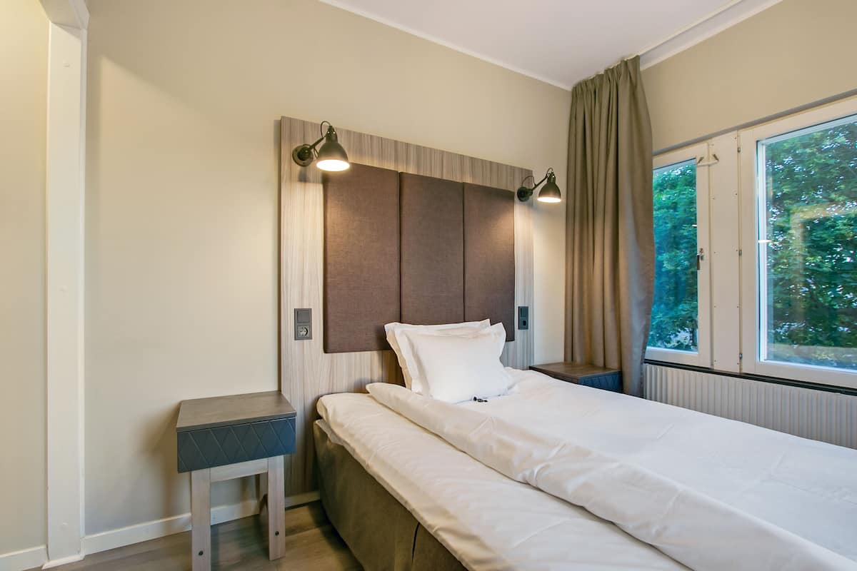 A bedroom with a bed, bedside tables, a headboard, and a window with a view of trees.