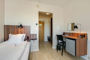 A hotel room with a bed, desk, chair, and a small refrigerator.