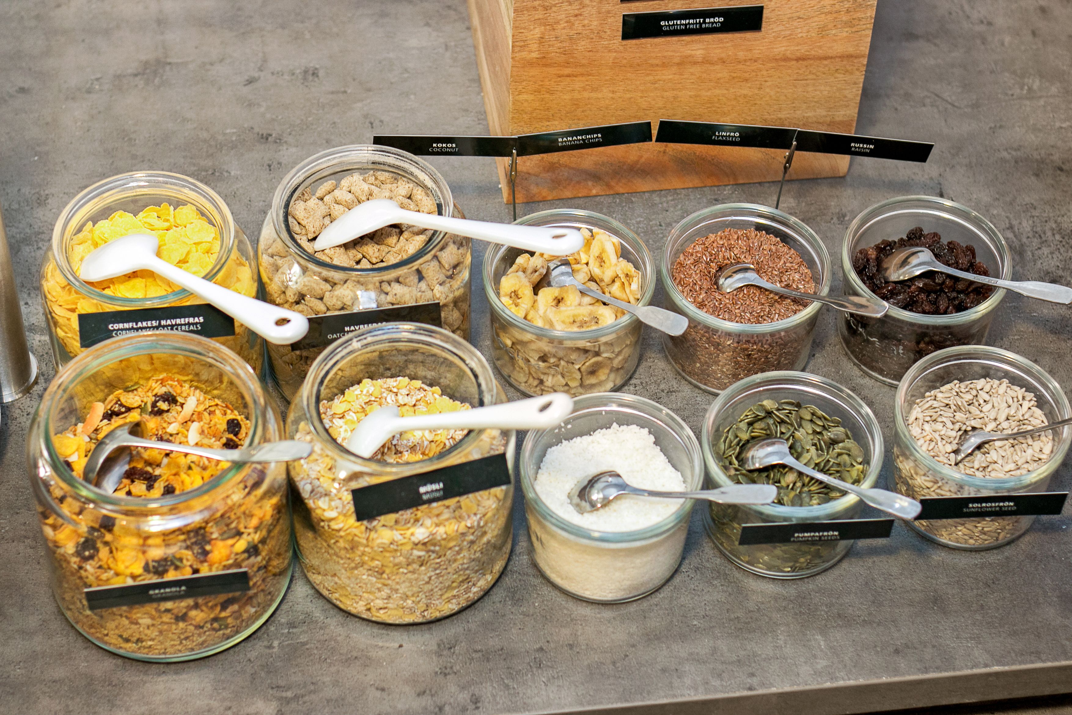 A variety of food items in glass jars with spoons, each labeled with different names.