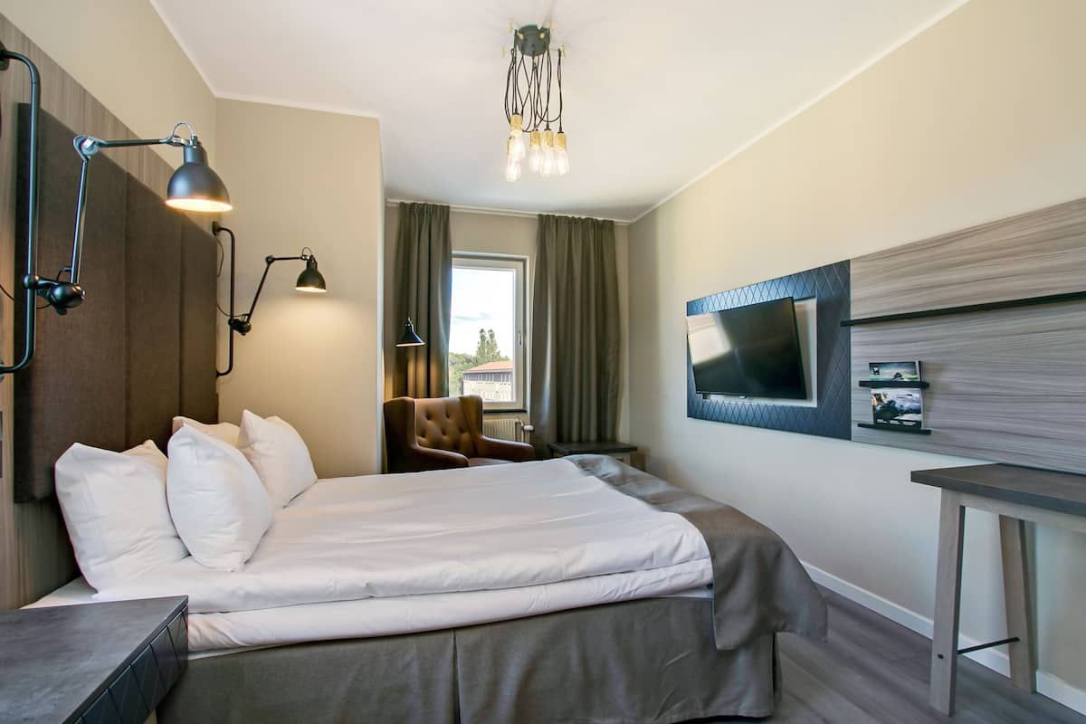 A hotel room with a bed, bedside lamps, a TV mounted on the wall, and a window with curtains.