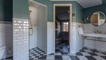 A bathroom with white subway tiles, a checkered black and white floor, a gold showerhead, and a white sink with gold fixtures.
