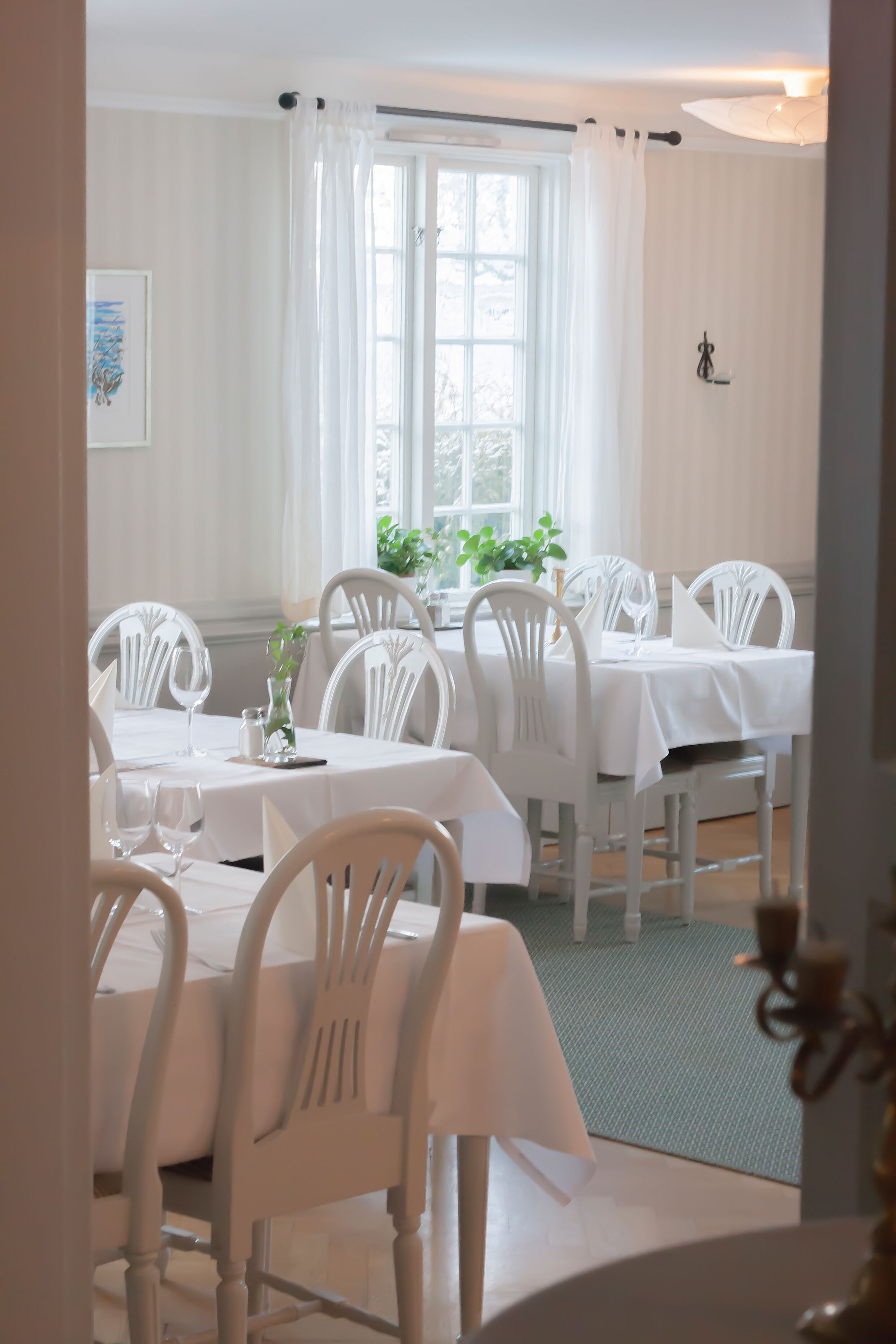 A dining area with white tables and chairs, a green rug, and a window with white curtains.