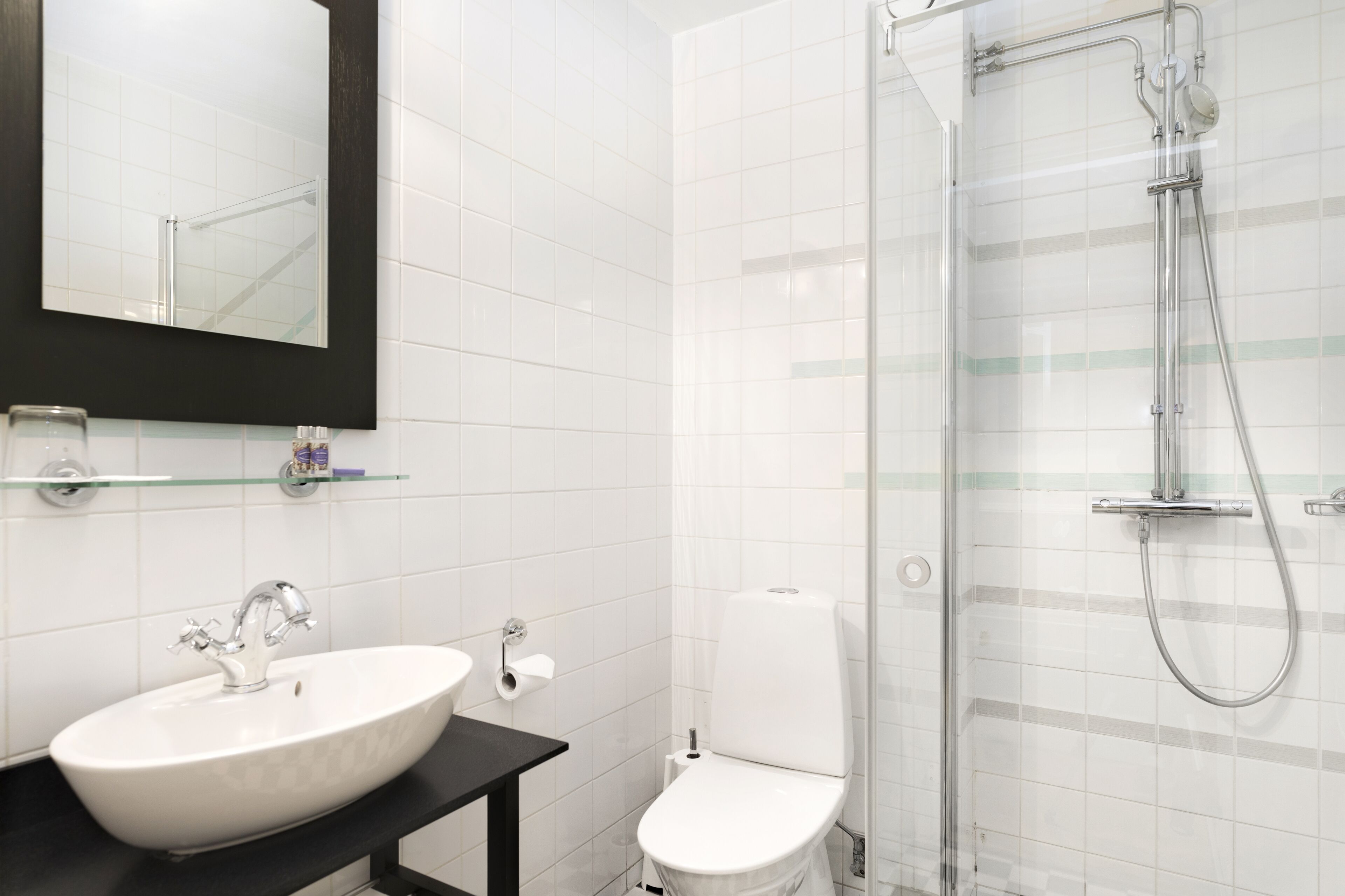 A modern bathroom with a white sink, black countertop, and a glass shower enclosure.