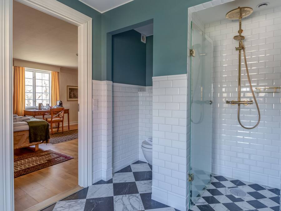Un baño con ducha, suelo de baldosas a cuadros y ventana con cortinas.