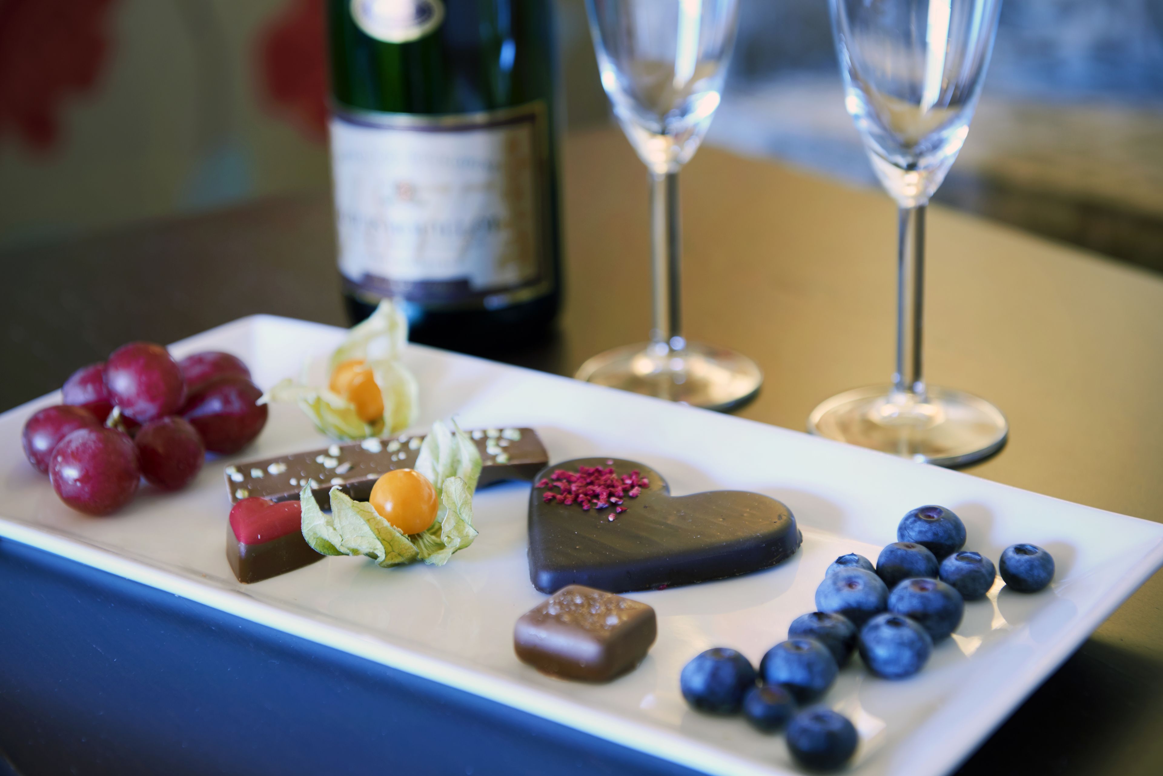 Un plat de postres amb diferents dolços, una ampolla i dues copes de vi.