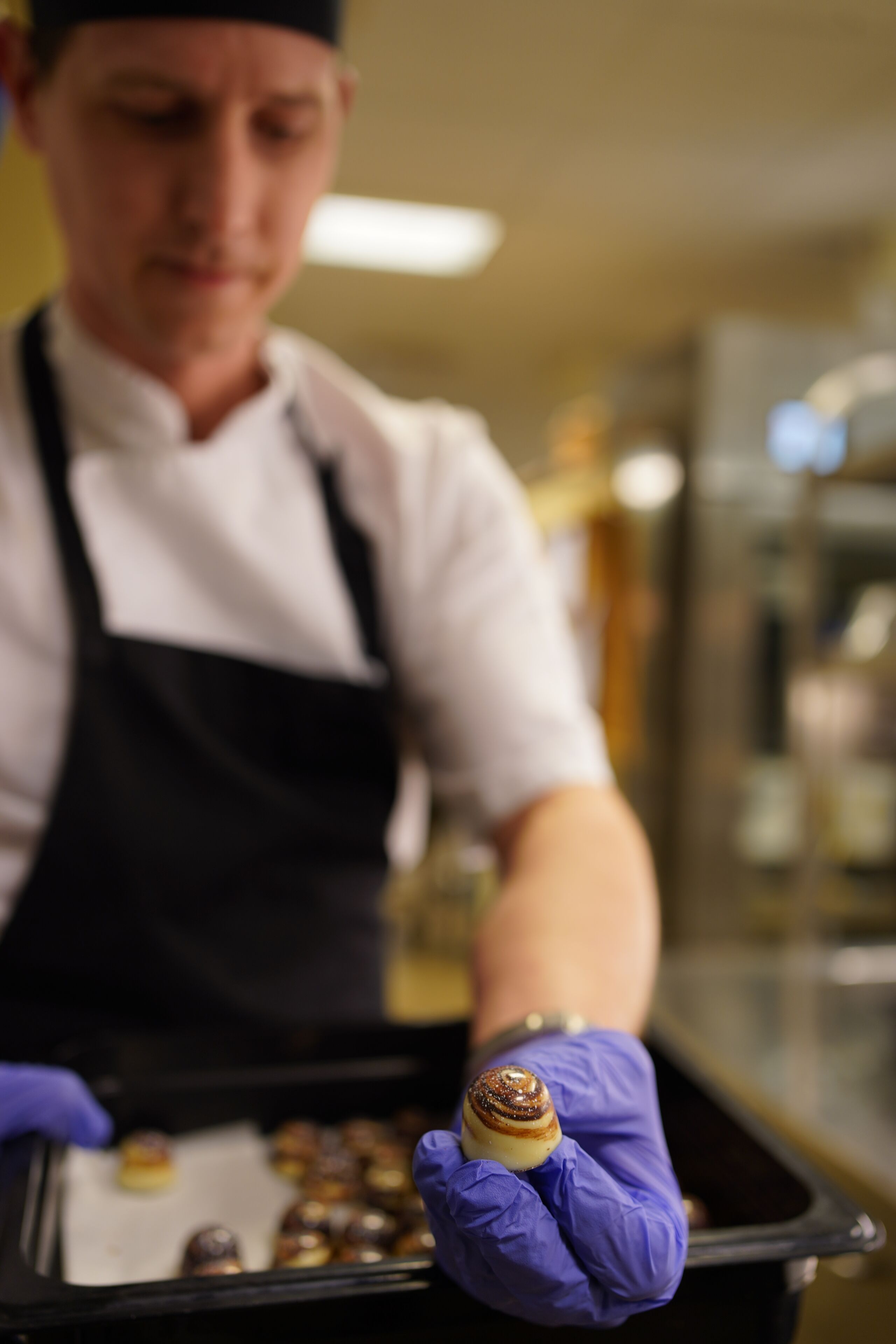 A chef in a white shirt and black apron holding a pastry.