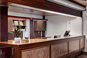 Un mostrador de recepción con detalles de madera, una planta en maceta y un diploma enmarcado.