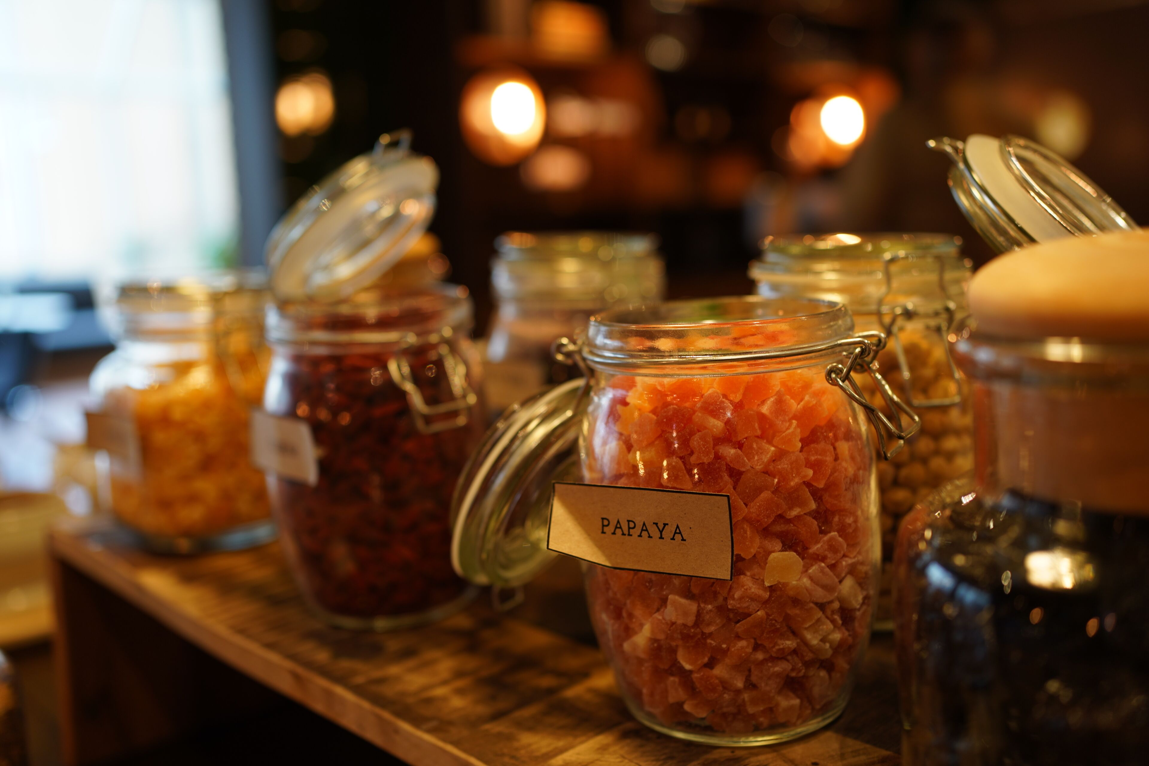 Une étagère en bois sur laquelle sont disposés plusieurs bocaux en verre, chacun étant étiqueté avec un nom et contenant probablement des aliments.