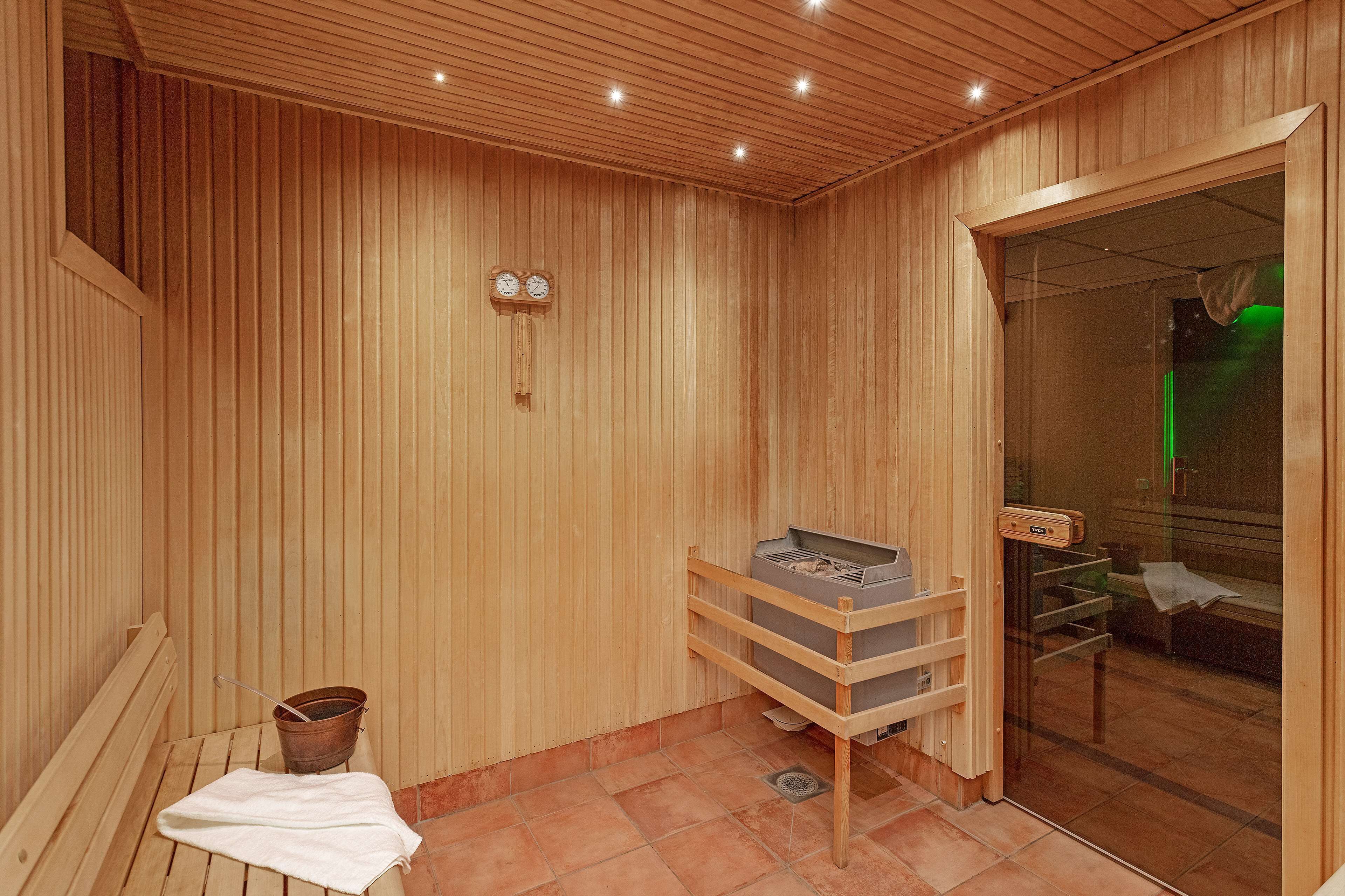 A wooden sauna room with benches, a wooden rack, a bucket, and a glass door leading to another area.