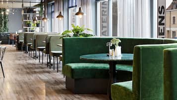 A restaurant with green upholstered booths, wooden flooring, pendant lighting, and large windows with curtains.