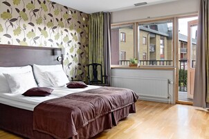 Un dormitorio con una cama grande, un radiador, una ventana con vistas a edificios y una cortina.