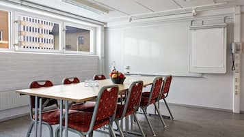 Un salón de conferencias con una larga mesa, sillas tapizadas de rojo, una pizarra blanca y una ventana con vistas a edificios.