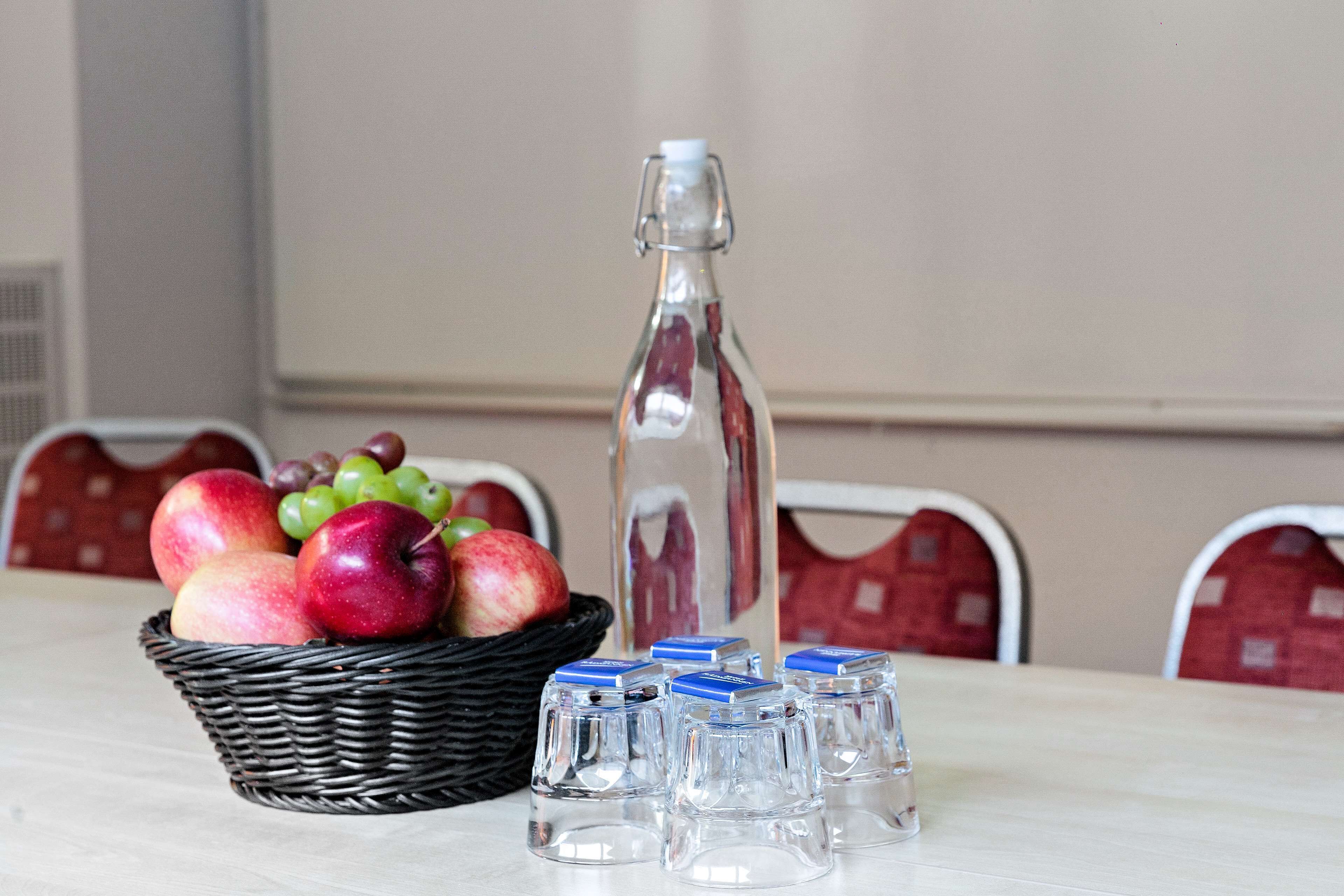 A table with a basket of apples and grapes, a bottle, and four glasses.