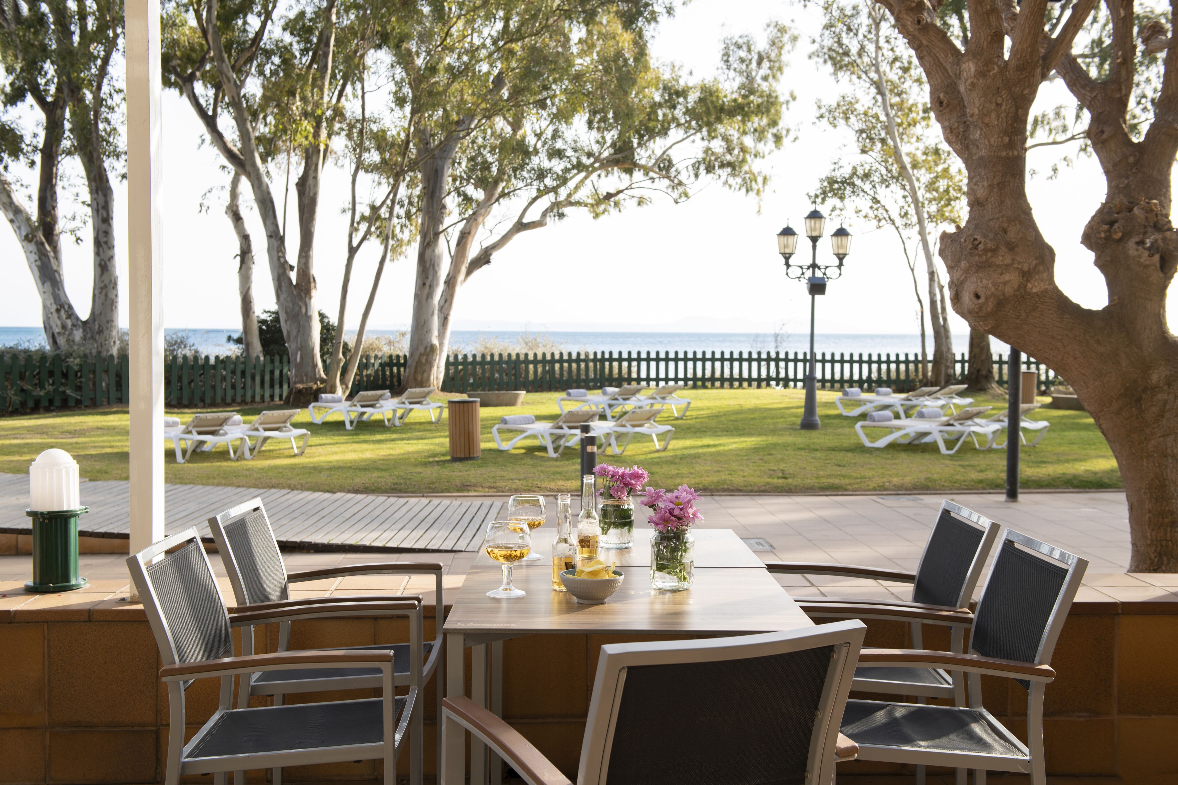 Un espace extérieur aménagé pour les repas, avec des tables et des chaises, une vue sur la mer et une clôture en bois en arrière-plan.