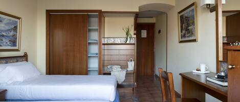 A hotel room with two beds, a desk, a chair, a small table, a bookshelf, and a bathroom visible through an open door.
