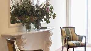 A room with two chairs, a mirror, and a vase with flowers on a console table. - Hotel Roses Platja (Roses)