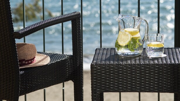 A wicker chair and table with a pitcher and glass on a balcony overlooking the sea. - Hotel Roses Platja (Roses)