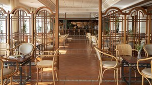 A spacious dining area with wooden chairs and tables, a central bar area, and large windows allowing natural light. - Hotel Roses Platja (Roses)