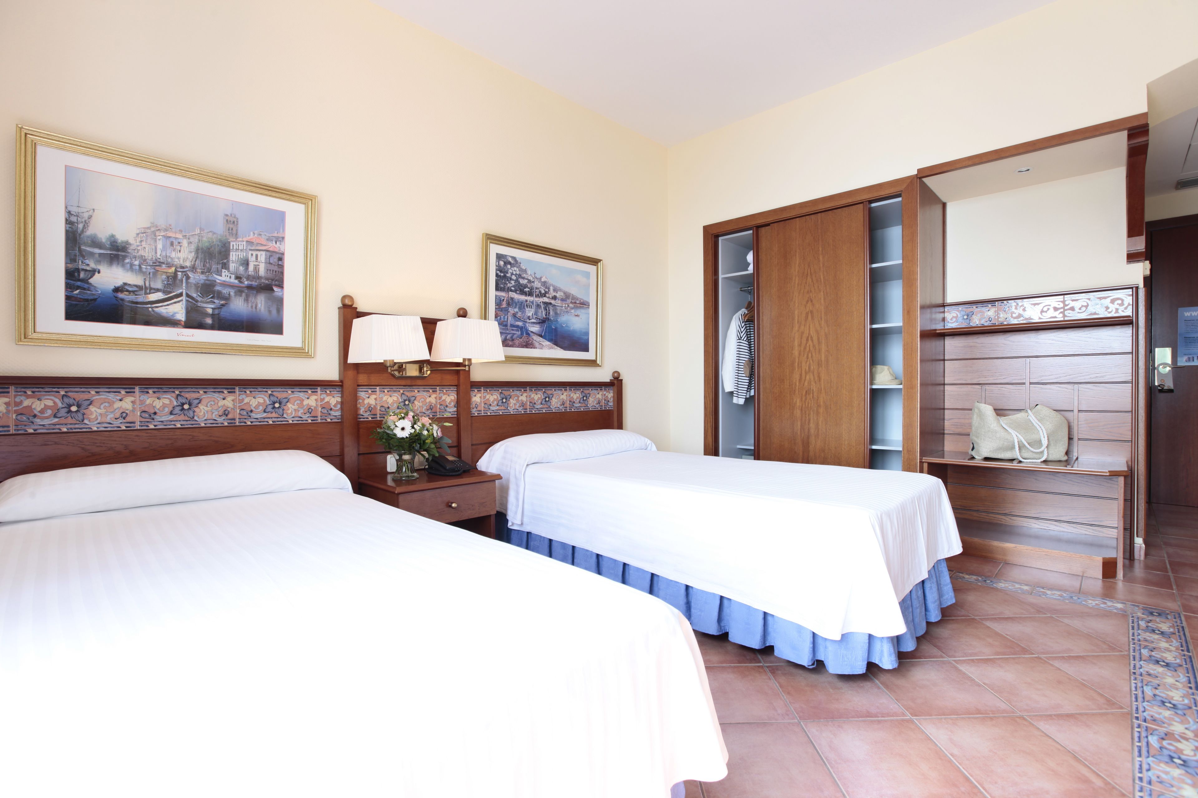 Een hotelkamer met twee bedden, een nachtkastje met lampen, een houten garderobe en een grote spiegel.