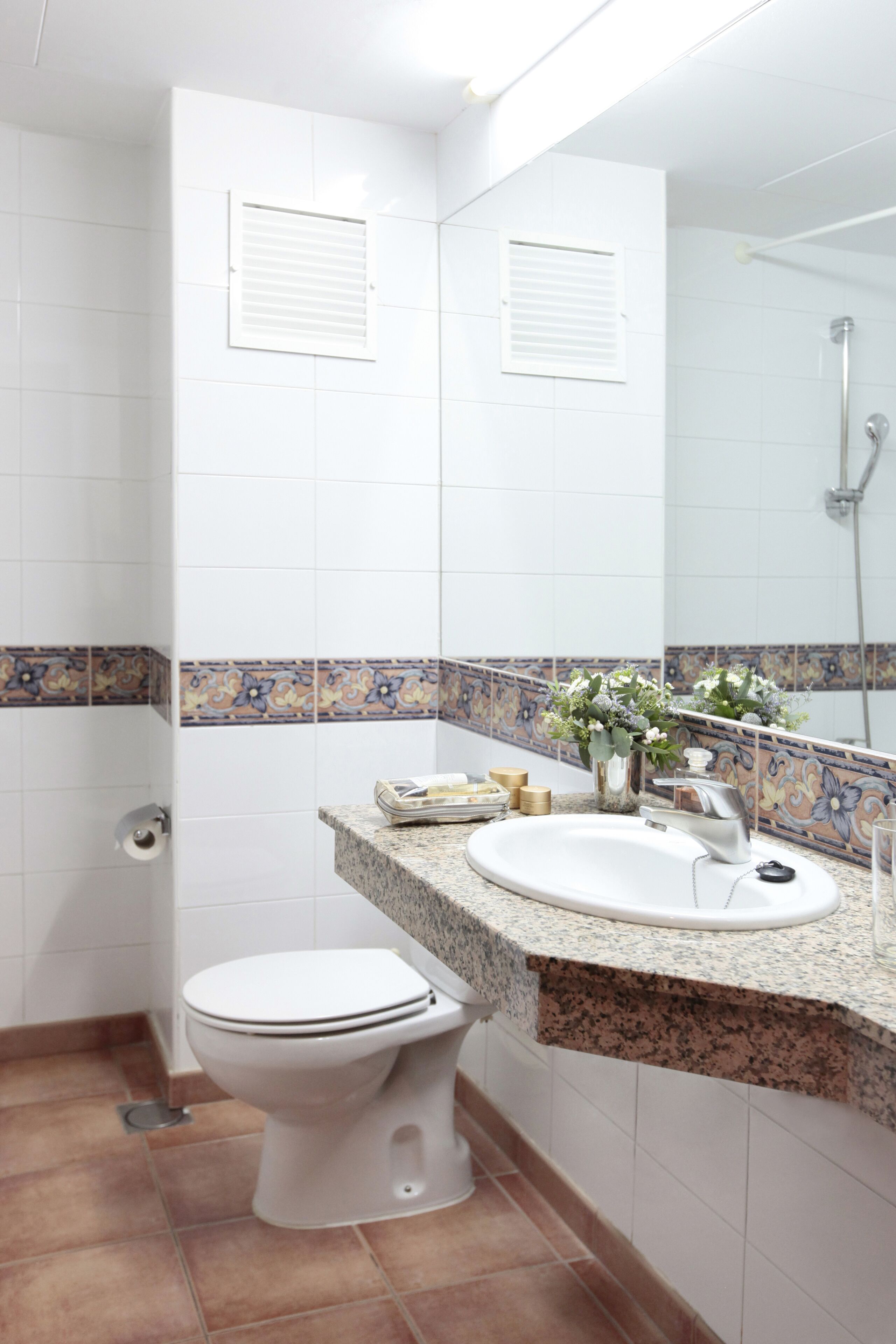 Une salle de bain avec des toilettes blanches, un lavabo avec un miroir au-dessus et un espace douche.