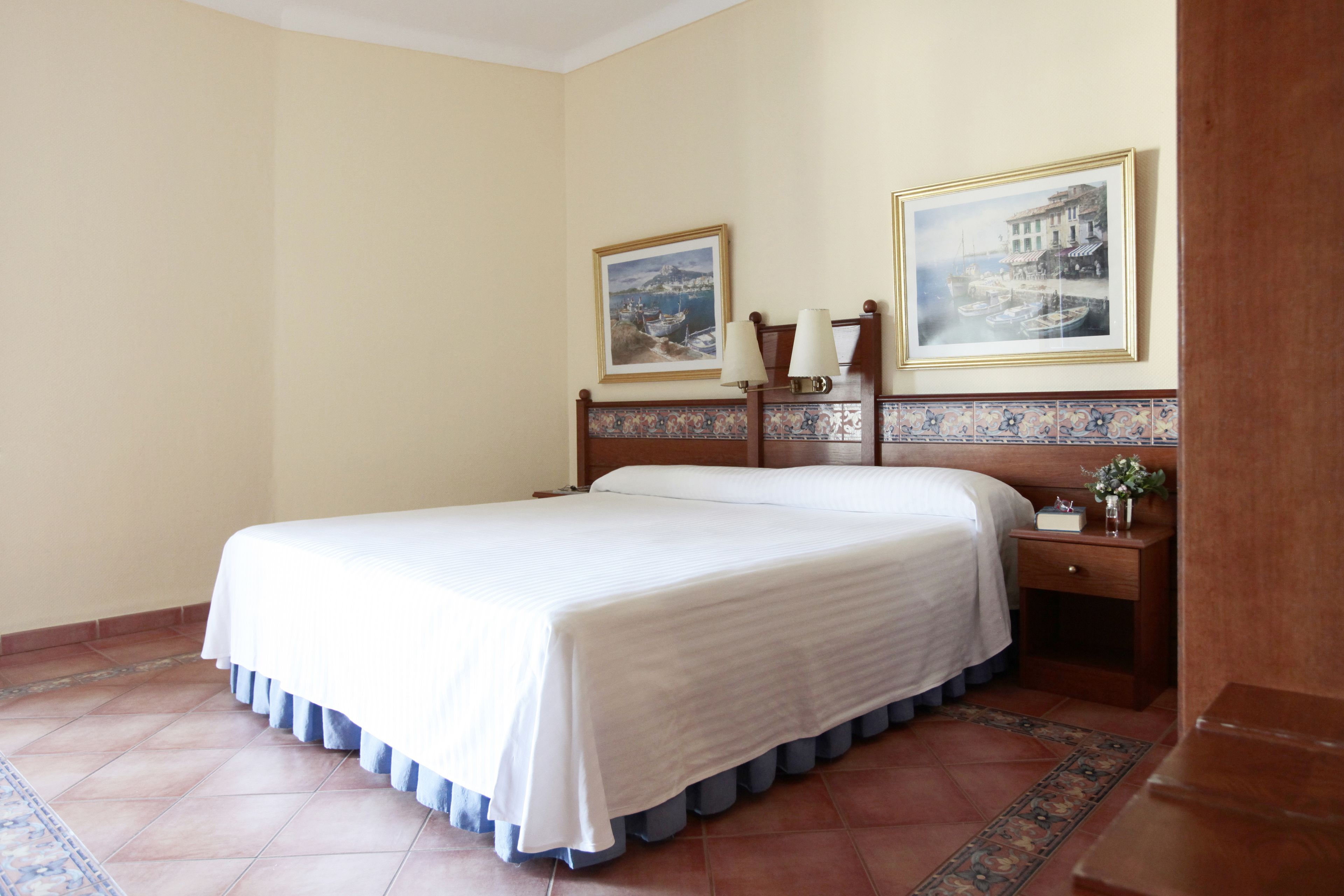 A hotel room with a large bed, two bedside tables, a nightstand, and two framed pictures on the wall.