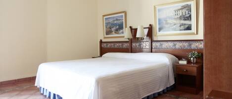 Une chambre d’hôtel avec un grand lit, deux tables de chevet, une petite table et deux tableaux encadrés au mur.