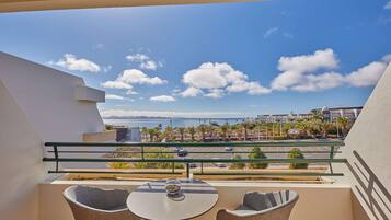 Un balcón con una mesa y dos sillas, con vistas a un aparcamiento, al mar y a edificios.