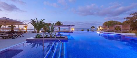 A pool area with lounge chairs and umbrellas, a clear sky, and a calm water surface.