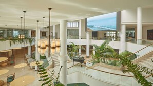 A spacious indoor area with multiple levels, featuring a central staircase, seating areas, and large windows overlooking a scenic view.