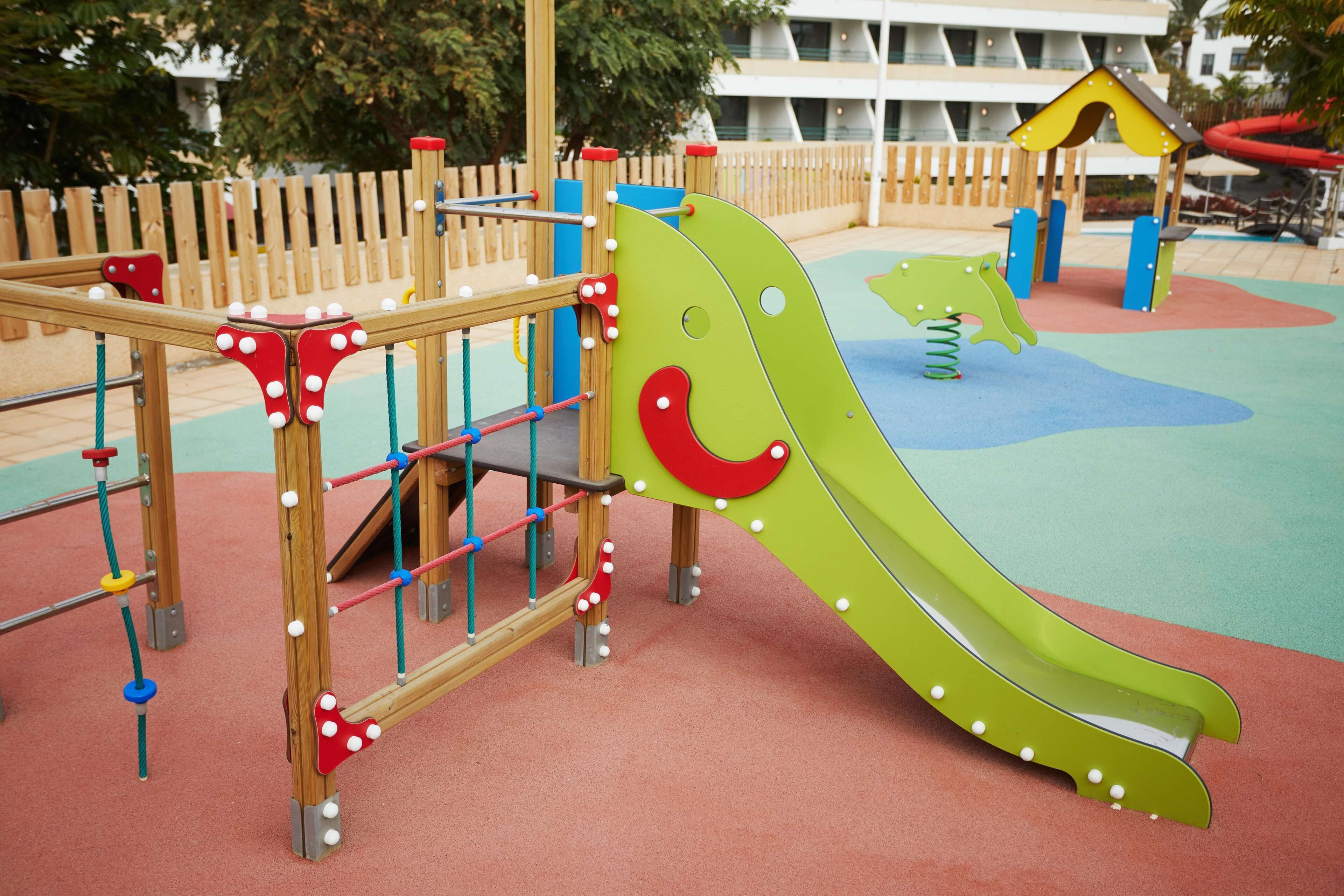 Un parque infantil con un tobogán, estructuras para escalar y una zona vallada.