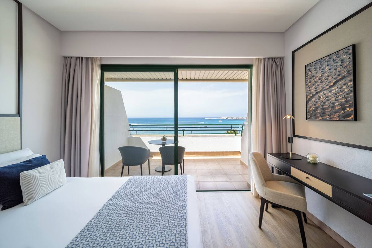 A hotel room with a bed, a desk, a chair, and a view of the ocean.