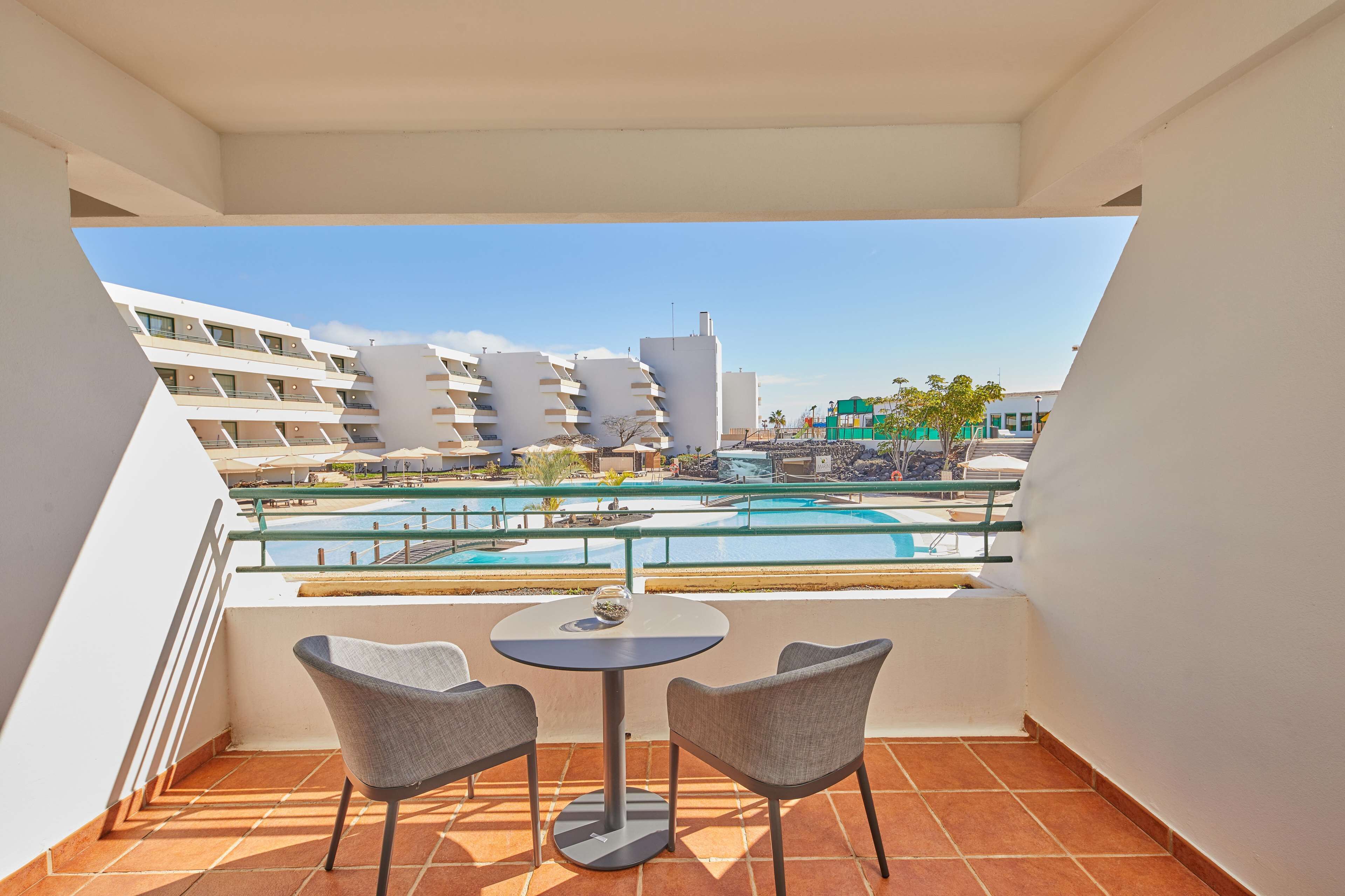 Un balcón con vista a la piscina, dos sillas y una mesa.
