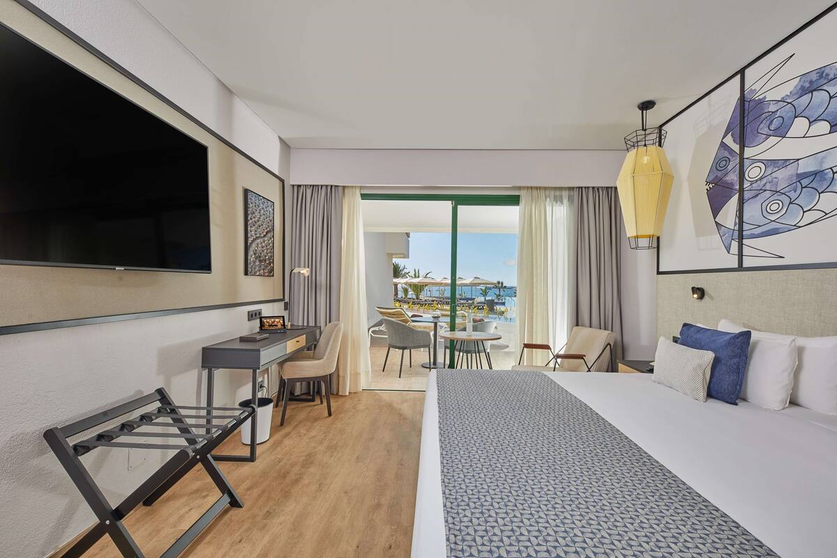 A hotel room with a bed, desk, chair, and a view of the pool and outdoor area.