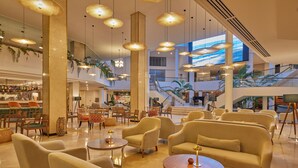 A spacious lobby with multiple seating areas, a staircase, and a large digital screen.