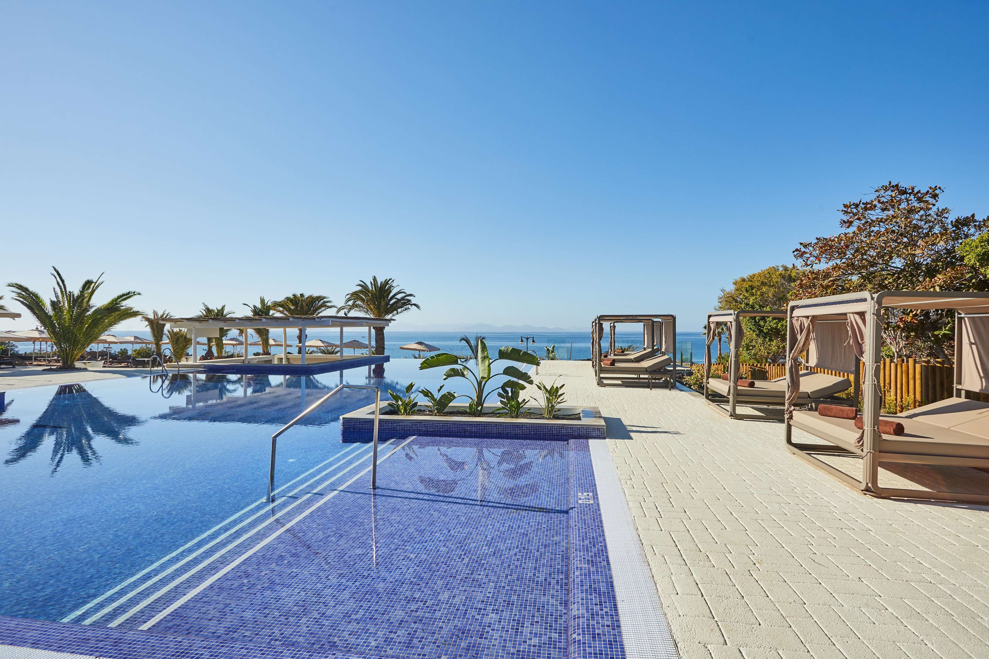 Une piscine à l’eau d’un bleu cristallin, entourée de chaises longues et de parasols, avec vue sur l’océan.